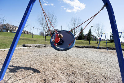 Boy playing on swing at park on sunny day