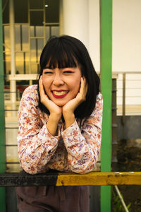 Portrait of smiling woman standing against railing