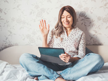 Woman on bed with tablet pc. she greets somebody via online video call. covid19 quarantine.