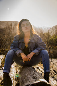 Portrait of young woman sitting on field against sky