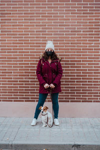 Woman with dog standing on footpath against wall