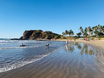 People on beach against clear blue sky