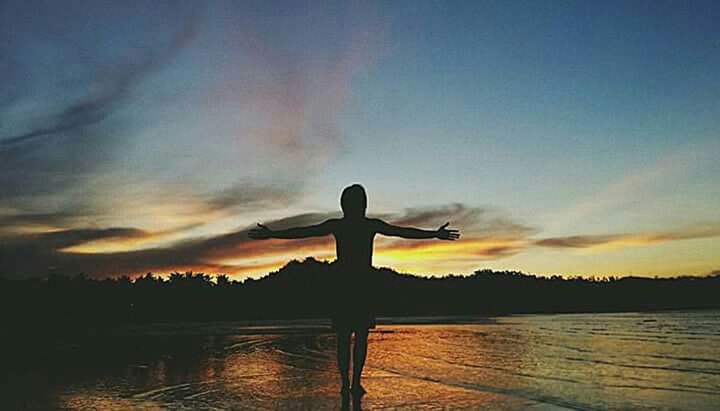 SILHOUETTE MAN STANDING BY LAKE AGAINST SUNSET SKY