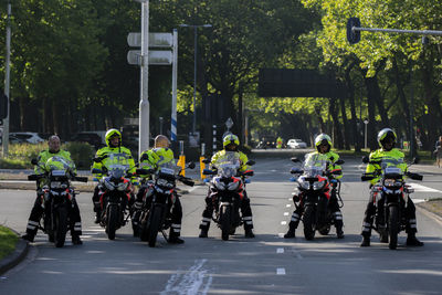 People riding motorcycle on street against trees in city