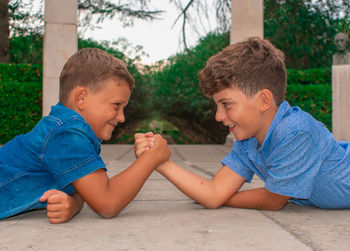 Friends arm wrestling while lying outdoors