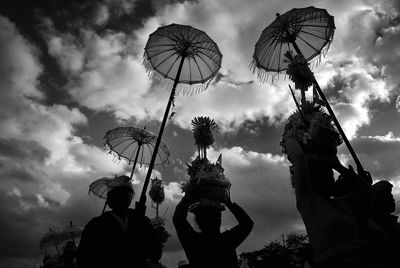 Low angle view of people with umbrella against cloudy sky during festival