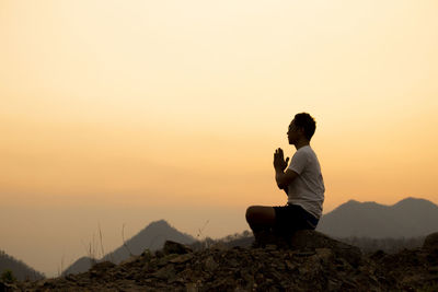 Man sitting on mountain against sky during sunset