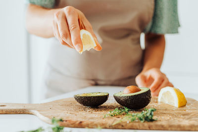 Female hands squeezing lemon while preparing a meal with avocado