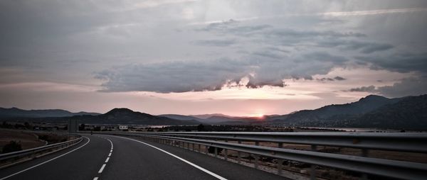 Road by mountains against sky during sunset