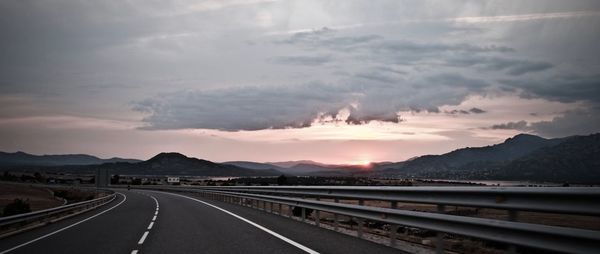 Road by mountains against sky during sunset