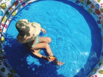 High angle view of girl wearing sun hat sitting in wading pool on sunny day
