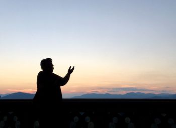 Silhouette of woman with arms raised against clear sky during sunset