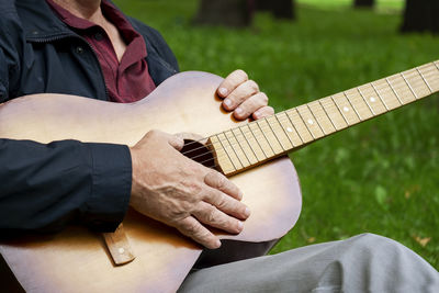 Adult romantic man sits in beautiful park on grass and holds six-string classical acoustic guitar