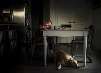 Girl coloring at dining table while dog lying on floor at home