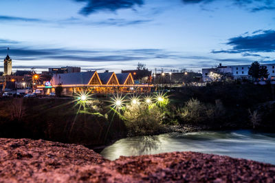Illuminated cityscape by river against sky at night