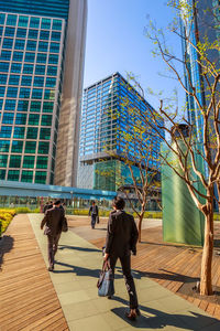 Rear view of people walking on footpath against buildings