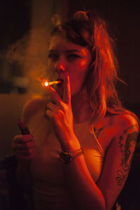 Portrait of young woman smoking in illuminated room