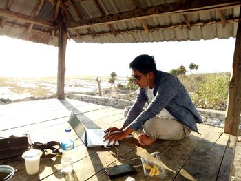 Side view of young man sitting at beach