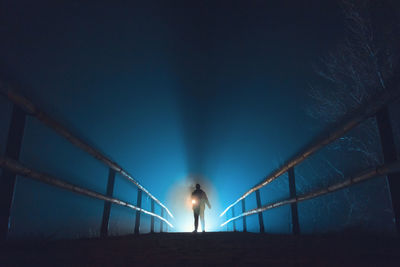 Person standing on illuminated pathway against sky at night