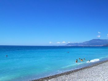 People enjoying at beach against blue sky