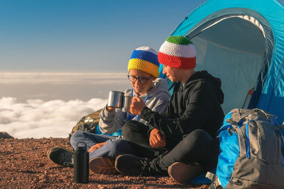 Brothers toasting coffee mugs while camping on mountain