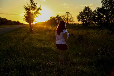 Rear view of woman standing on field during sunset