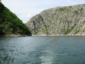 Scenic view of sea by mountain against sky