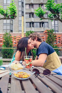 Man whispering in woman ear by food and drink at restaurant