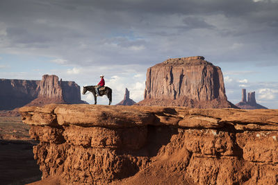 Man sitting on horse at desert against cloudy sky