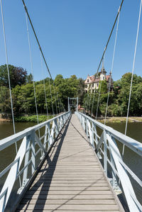 Footbridge over river against clear blue sky