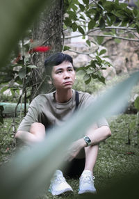 Portrait of young man with arms raised standing against trees