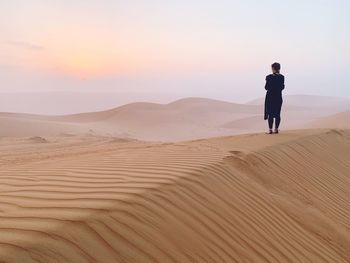 Man standing on sand dune in desert against sky