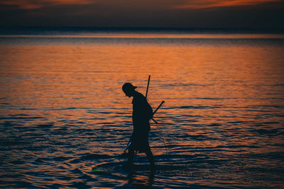 Silhouette man wading in lake against sunset sky