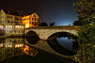 Arch bridge over river amidst buildings in city at night