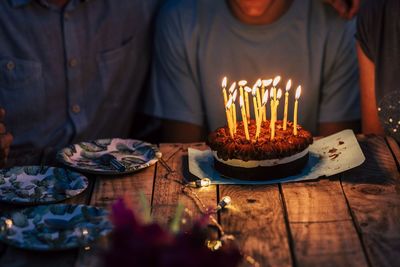 Midsection of man sitting by birthday cake