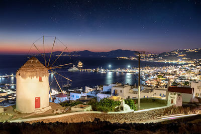 Illuminated buildings by sea against sky at night