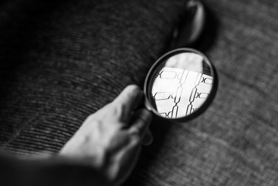 Cropped image of hand holding magnifying glass over book