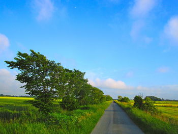 Empty road amidst field against sky