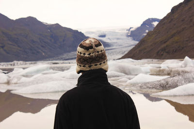 Rear view of man standing in front of snow covered mountains