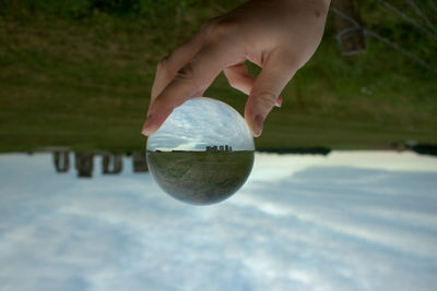 Close-up of hand holding crystal ball against sky