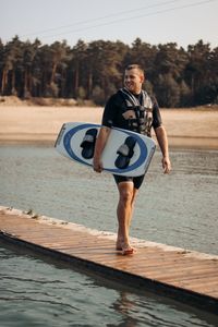 Full length of young man holding surfboard walking on pier