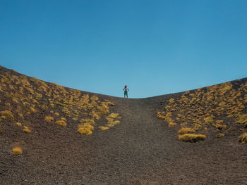 Distant view of mature woman with arms outstretched standing on mountain against clear blue sky