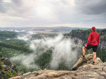 Runner in pink jacket and light black shorts. short ginger hair man on the path in rocky mountains.