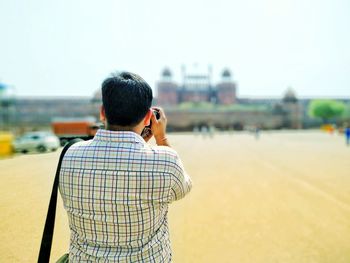 Rear view of man photographing historic building while standing on street in city