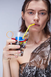 Portrait of young woman drinking water with plastics in glass