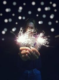 Portrait of mid adult woman holding sparklers while standing outdoors at night