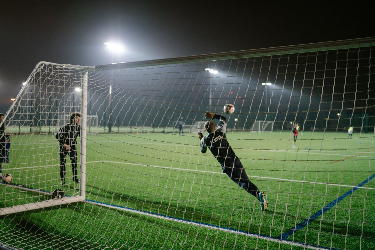 sport, team sport, soccer, grass, competition, playing, night, net - sports equipment, soccer field, football, playing field, competitive sport, illuminated, sports equipment, group of people, soccer goal, leisure activity, men, real people, large group of people, outdoors, goalie, effort