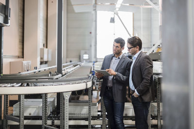 Two businessmen with tablet talking at conveyor belt in factory