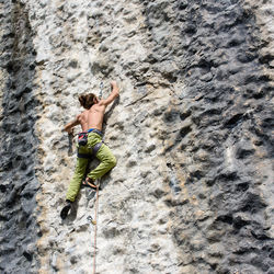 Rear view of shirtless man climbing on rock