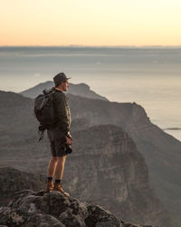 Side view of backpacker looking at landscape while standing on cliff during sunset